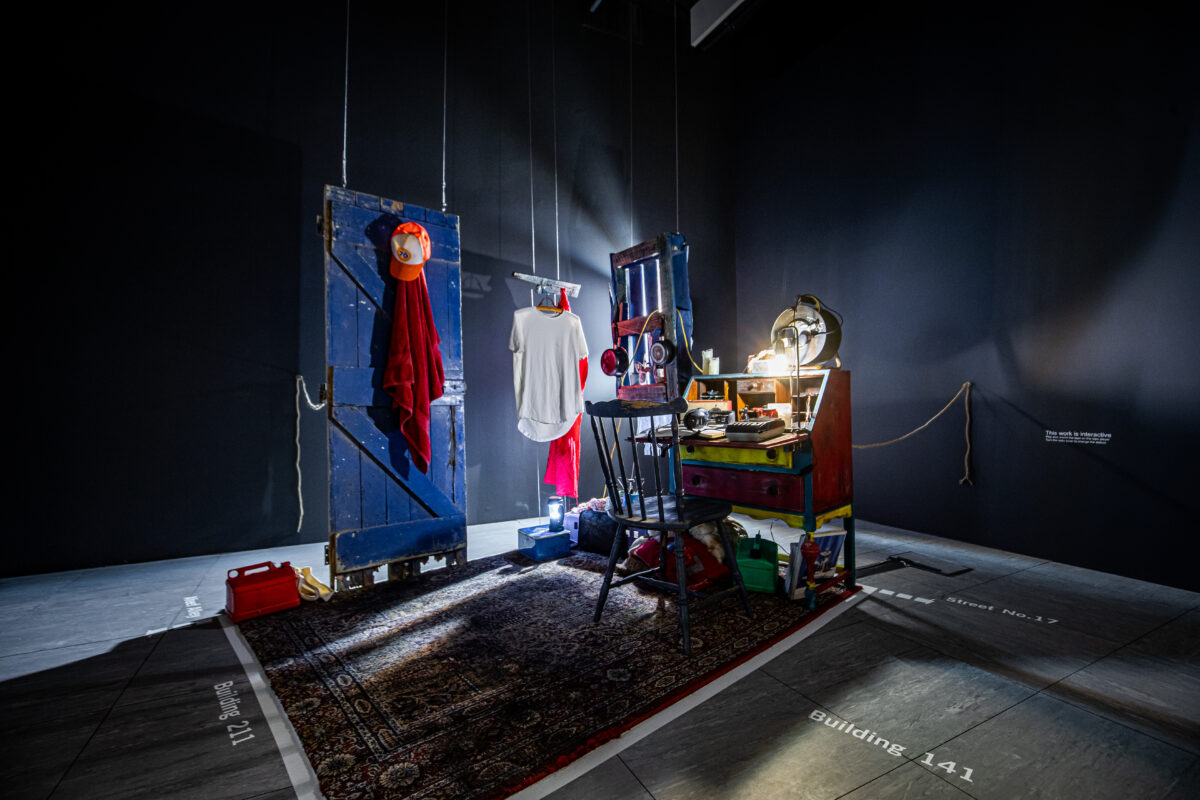 Installation view of The Diary. A small room is staged on a carpet, with a bright light on a desktop.